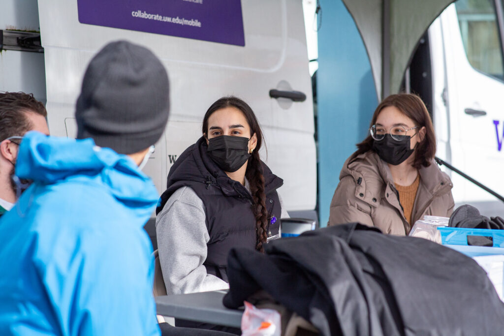 Four students sit around a table in front of a Mobile Health Van.